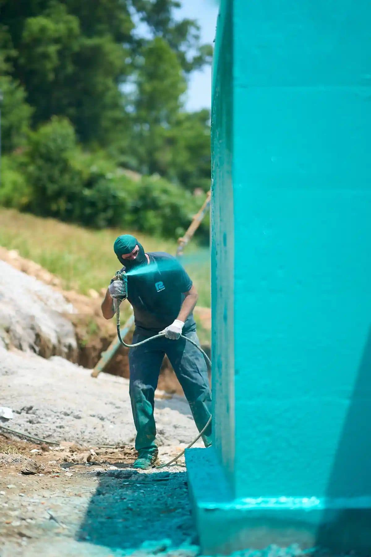 Spray application of teal Rub-R-Wall membrane on a foundation wall